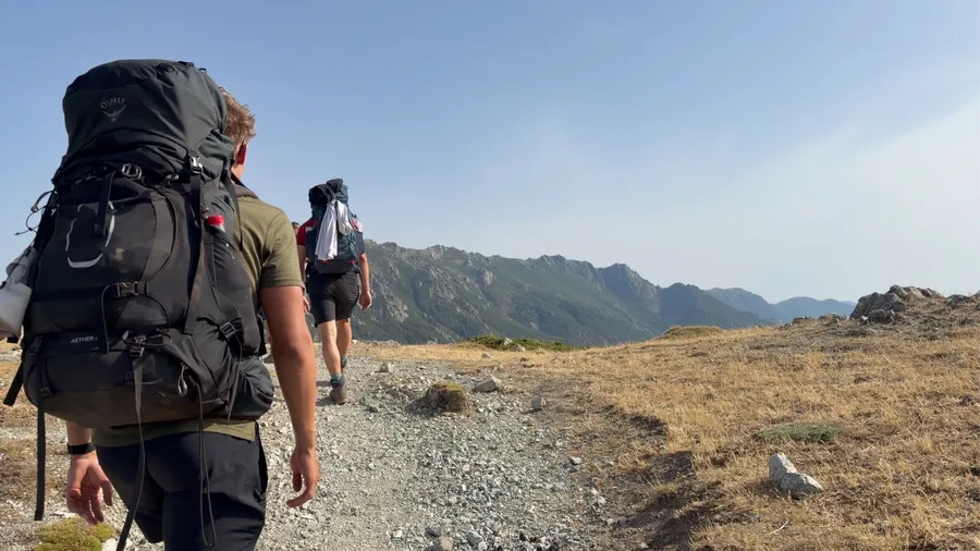 Wanderer mit großem Rucksack auf dem GR20, dahinter die Berge Korsikas